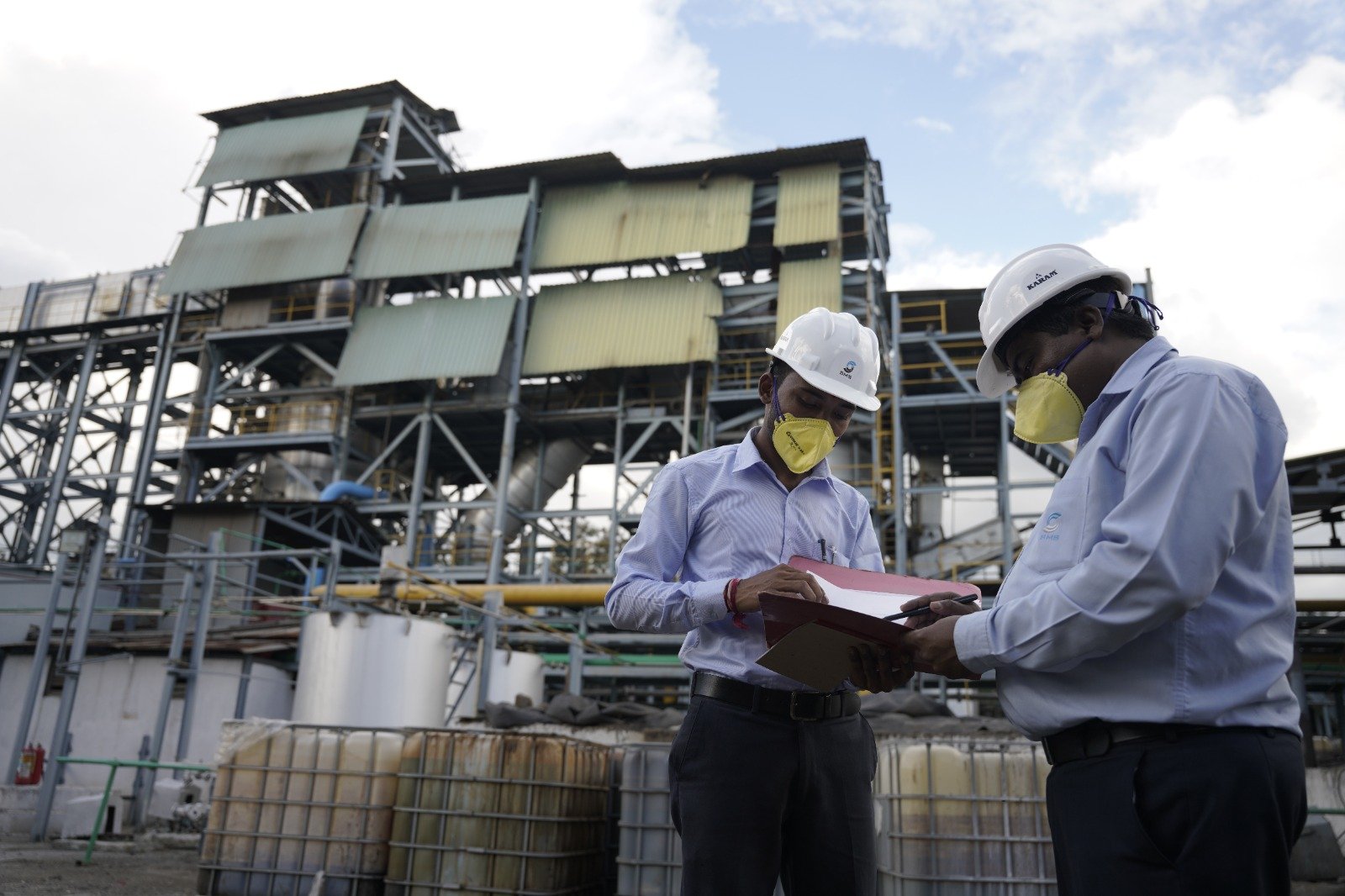 Industrial Waste Facility Safety Inspection SMS Envocare engineers wearing helmets and masks reviewing safety documents at an industrial hazardous waste treatment facility.