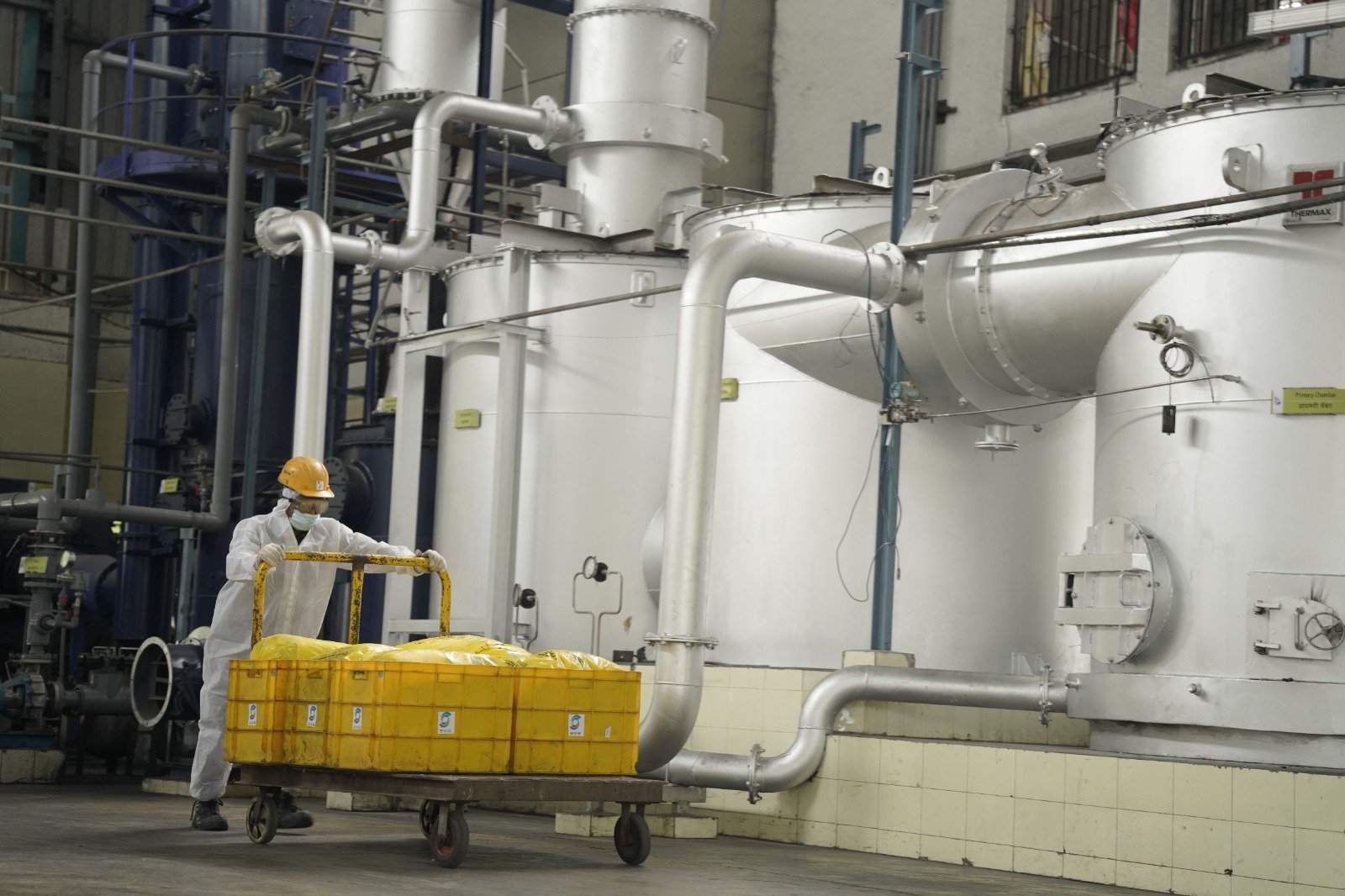Bio-Medical Waste Material Handling SMS Envocare operator in protective gear moving yellow bio-medical waste containers near treatment chambers.
